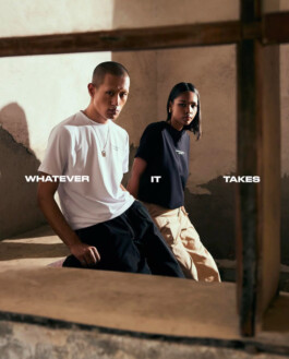Sachit Gurung and a female model pose in minimal white and black T-shirts inside a rustic concrete space, framed by a window, with bold text reading “WHATEVER IT TAKES.” 