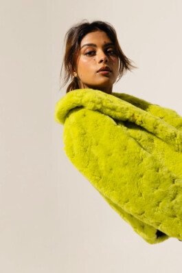 Model Natascha Mehra wearing a neon green faux fur coat with glitter stars on her face, posing in studio light against a neutral background 