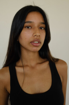 Model Dipannita Bhuyan in a natural light studio portrait, wearing a black tank top with minimal makeup and clean, straight hair. 