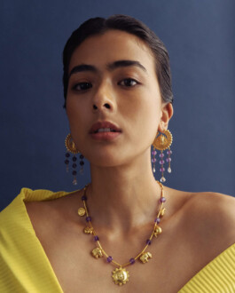 Medhavi Chettri wearing ornate gold and amethyst earrings and necklace for Olio jewelry campaign, styled in a yellow pleated outfit 