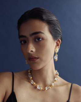 Medhavi Chettri wearing crystal bead necklace and gold sunburst earrings for Olio campaign against a navy background 