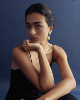 Medhavi Chettri wearing gold drop earrings and black dress for Olio campaign against navy backdrop 