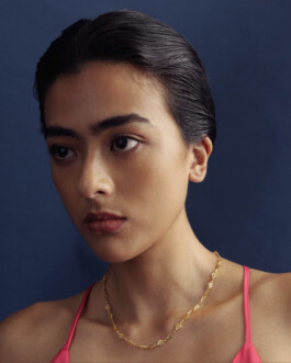 Medhavi Chettri wearing a delicate gold chain necklace and pink top for Olio campaign with navy backdrop 