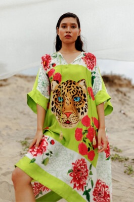 Merrylin Boro wearing a lime green silk kaftan with a bold leopard face motif and red floral accents by Verandah, posing on a sandy beach 