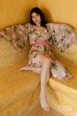 Merrylin Boro reclining in a pink floral Verandah kimono dress with flared sleeves against a yellow stone bench 