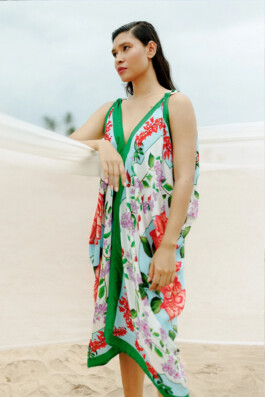 Merrylin Boro wearing a vibrant floral kaftan-style beach dress by Verandah, standing against a sandy beach backdrop 