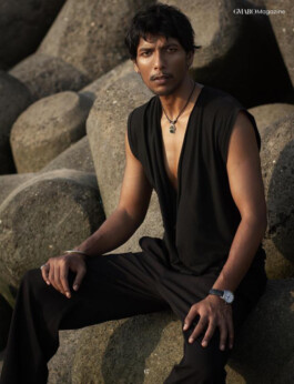 Male model Gaurav Gharu poses in a sleeveless black outfit on rocky tetrapods during golden hour for GMARO Magazine editorial 