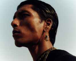 Close-up side profile of Gaurav Gharu wearing a sculptural earring and layered gold necklaces under natural light 