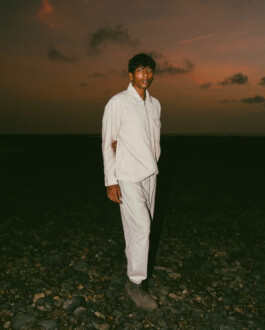Model Gaurav Gharu standing on a rocky beach at sunset in a light outfit 