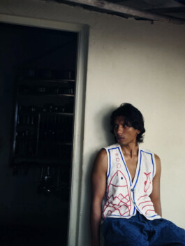 Model Gaurav Gharu wearing a white sleeveless vest with red fish embroidery and blue detailing, styled with blue trousers for Fenmy Taxena campaign 