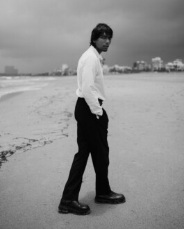 Black and white full-length image of ALF model Gaurav Gharu walking along the beach in tailored black pants and white shirt 