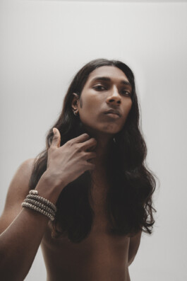 Model Savio Fedrick in a bare-shouldered close-up with long hair and silver bracelets, photographed by Ambika Singh 