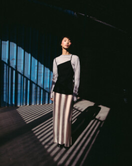 Model Tenzin Martha stands in a dramatic play of light and shadow wearing a two-tone slip dress layered over a grey top, photographed for A Little Fly modeling agency India 