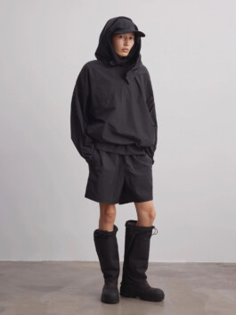 Ngawang Jinpa wears a hooded black windbreaker, matching shorts, cap, and knee-high boots in a minimal studio fashion shoot for A Little Fly 
