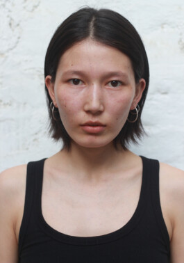 Clean beauty digital portrait of model Ngawang Jinpa wearing a black tank top and silver hoop earrings against a neutral background. 