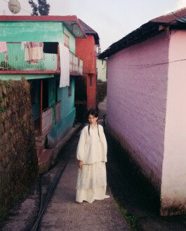 Ngawang Jinpa wearing an off-white embroidered set, standing in a narrow lane between colorful houses for the Eka campaign, photographed by Tenzin Lhagyal. 