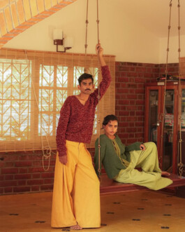 ALF model Ishra Philipose seated on a traditional indoor swing in a sunlit room with exposed brick, styled in oversized green knitwear and wide-leg trousers for the Kula Campaign 