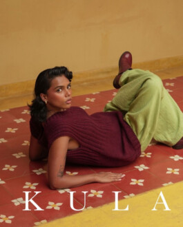 ALF model Ishra Philipose poses on a tiled floor wearing a burgundy sweater vest and green trousers for the Kula fashion campaign 