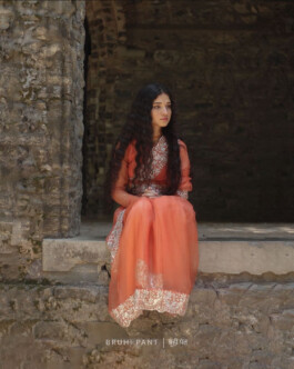 Deepika Sagar, ALF model, in an orange embroidered outfit sitting by a stone arch for the Bruhi Pant campaign 