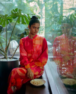 Aakriti Tyagi in a red floral dress sitting by a window for the Norn fashion campaign 