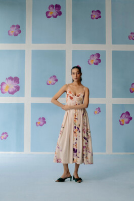 Akriti Jha wearing a peach floral midi dress, posing gracefully against a blue floral backdrop for Uri 