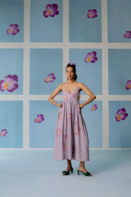 Akriti Jha poses in a lavender floral midi dress against a pastel flower wall for Uri campaign 