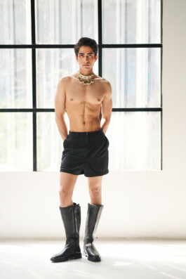 Male model Siddharth Raghavan posing shirtless in black shorts and boots with a traditional Indian necklace 