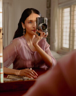 Anushree Vaze holding a vintage camera while wearing statement jewellery for Moi campaign, reflected in a mirror 