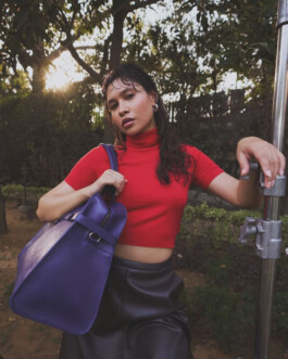 Model Merrylin Boro in a red top and leather skirt holding a purple Mistry handbag during a golden hour outdoor campaign shoot 