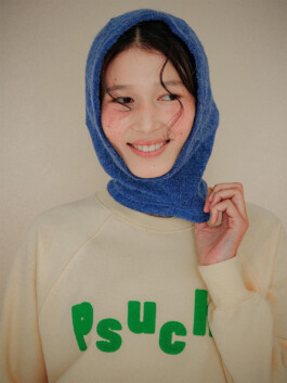 Ngawang Jinpa smiling in a cream sweatshirt with green Psuche lettering and a blue hood 