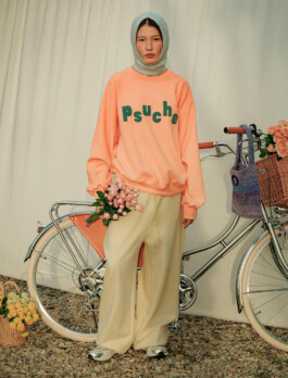 Ngawang Jinpa wearing a peach Psuche sweatshirt and holding flowers, standing beside a bicycle for ALF India 