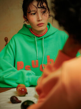 Ngawang Jinpa wearing a green psuche hoodie and coral bead necklace at a dining table 