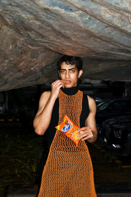 Model Siddharth Raghavan in black and orange net outfit holding Kurkure during test shoot 