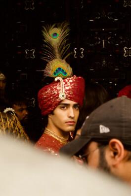 Siddharth Raghavan wearing an ornate red turban with peacock feathers backstage during an Itrh campaign, represented by ALF – A Little Fly, one of the best modeling agencies in India. 