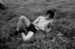 Black-and-white editorial photograph of male model Aaditya Yadav reclining shirtless in a grassy field, showcasing his lean frame and expressive presence; represented by ALF – A Little Fly, one of the best modeling agencies in India. 