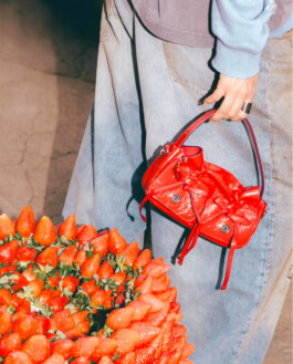 Close-up of a red Acne Studios handbag next to a vibrant basket of strawberries, photographed by ALF’s Tito for Ajio 