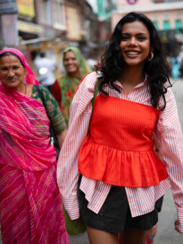 Ishra Philipose smiling in striped shirt and orange top, walking alongside Rajasthani women in bright sarees – Wasala campaign 