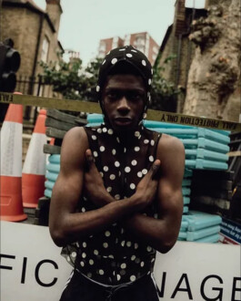 Black model in sheer polka dot top and hood posing against an urban construction backdrop, photographed by Tuhin Chandra 