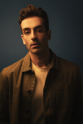 Editorial portrait of male model Vikas Mandaliya in warm cinematic lighting against a dark blue background. 