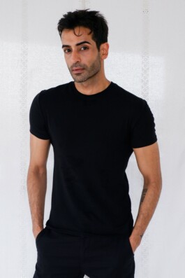 Indian male model Vikas Mandaliya standing against a white backdrop in a black t-shirt with hands in pockets 