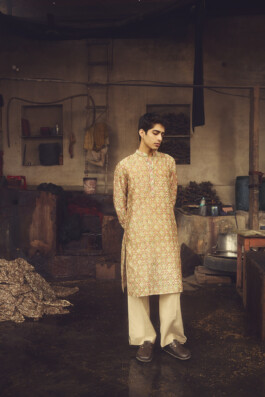 Model Siddharth Raghavan wearing a traditional printed kurta in a rustic dyeing or block printing workshop, surrounded by artisan tools and fabric 
