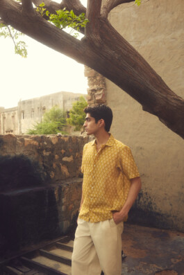 Model in mustard block print shirt and cream trousers standing by stone ruins and tree, captured for House of Tuti fashion campaign 