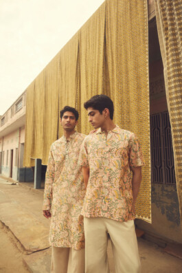 Models wearing pastel floral Indian menswear posing against printed fabric backdrops in traditional street setting for House of Tuti campaign 