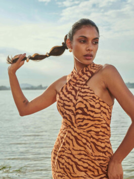 Shweta Poothery holding her braided hair while wearing a brown tiger print Elisamama dress by the water 