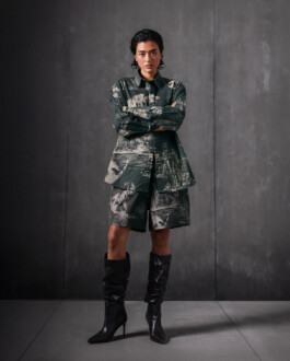 Medhavi Chettri, represented by ALF modeling agency, in the Almost Gods campaign wearing a printed oversized shirt with matching shorts and black heeled boots against a dark minimalist backdrop. 