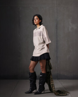 Medhavi Chettri, represented by ALF modeling agency, poses in a contemporary streetwear-inspired look featuring a beige oversized polo, black mini skirt, and high-heeled boots for the Almost Gods campaign. 