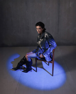 Medhavi Chettri, represented by ALF modeling agency, seated under a dramatic blue spotlight in the Almost Gods campaign, wearing an oversized printed shirt with high black boots. 