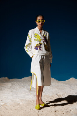 Model Akriti Jha wearing a white dress with vibrant embroidered frog motifs, styled with yellow shoes and sunglasses, for Mohammed Mazhar Jungle Dress campaign 