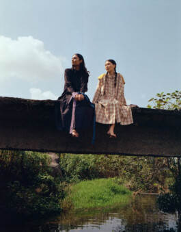 Two models seated on a bridge above a stream wearing Eka dresses during a campaign shoot photographed by Tenzin Lhagyal for ALF. 