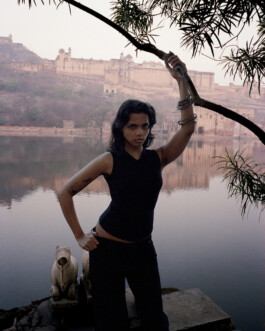 Female model in a black tank posing by a lakeside with historic architecture in the background for Tank Air campaign, styled in an outdoor editorial setting. Represented by ALF – A Little Fly, a leading modeling agency in India 